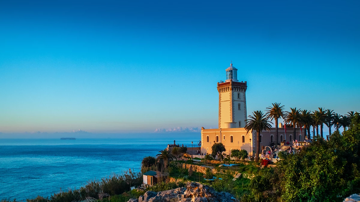 Phare du Cap Spartel au coucher du soleil avec des palmiers et vue sur l’océan à Tanger, Maroc